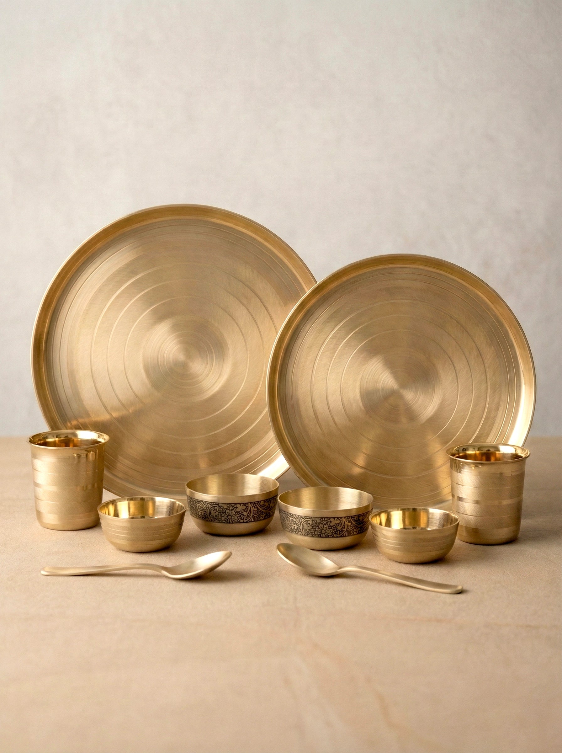 Set of bronze dinnerware including plates, bowls, and cups on a beige surface.