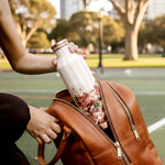 Person holding a copper water bottle with a blurred park background