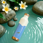Blue and white patterned copper bottle with copper cap on a water surface with stones and flowers